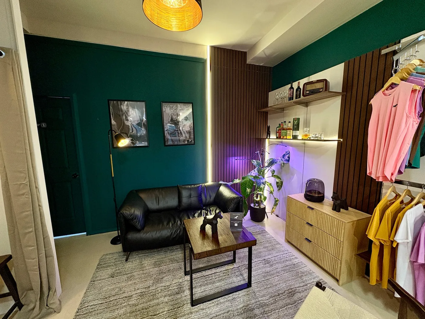 El Lounge del Perro: sillón de cuero negro frente a una pared verde, mesa de madera con un perro de origami y un bar con whisky y copas junto a la ropa
